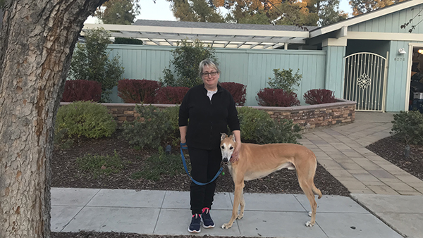 Woman standing with greyhound dog in front of a house