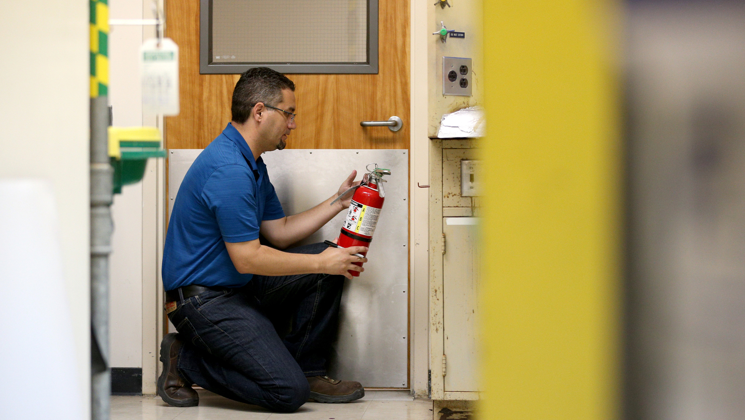 Male employee kneeling in front of a door looking at a fire extinguisher