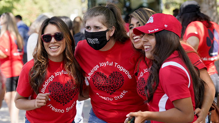 Four women smiling for photo wearing red Bulldogs Joyful Together Fresno State shirts
