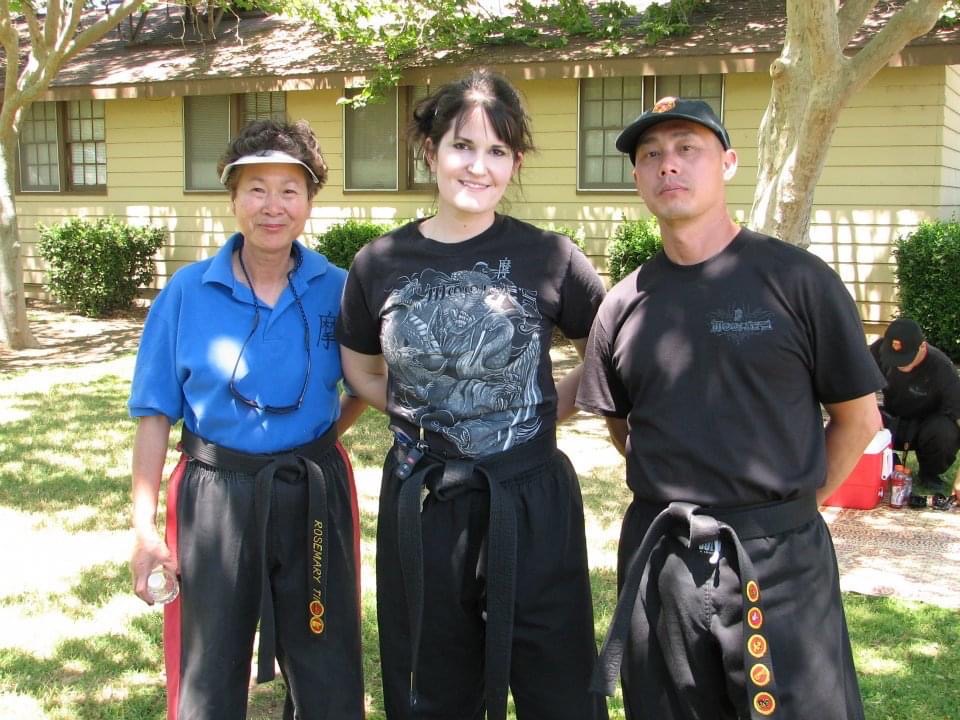 Meredith Sandrick, with her black belt, stands with two people.
