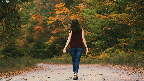 Woman walking on a path in the woods. Trees are green, yellow and red.
