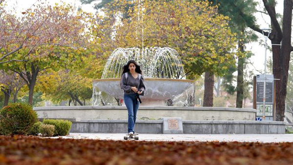Female student on skateboard in front of fountain.