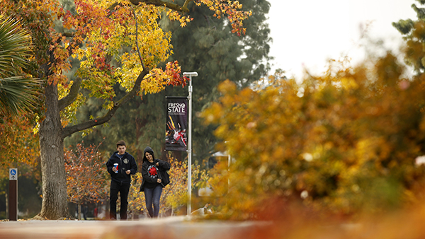 Two students walking through the Fresno State campus during fall time.