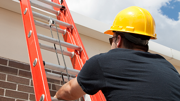 Man in yellow hardhat climbing a ladder to the roof of a building