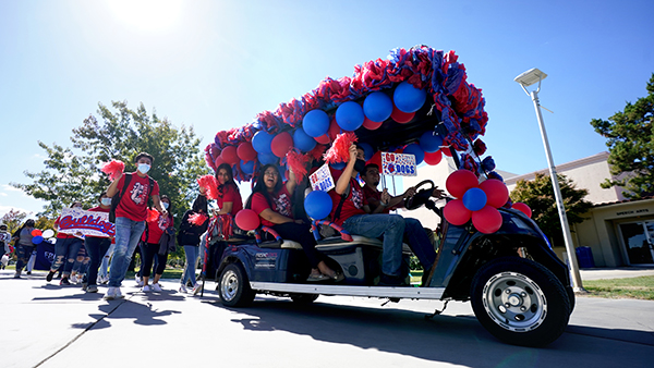 Golf cart decorated with blue and red balloons and filled with staff and students.