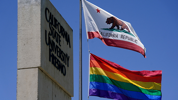 California flag and rainbow pride flag flying next to a California State University Fresno sign.
