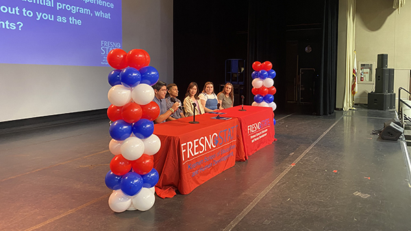 Speakers sitting at a table on stage in the Satellite Student Union. The table is bookended with red, white and blue balloons.