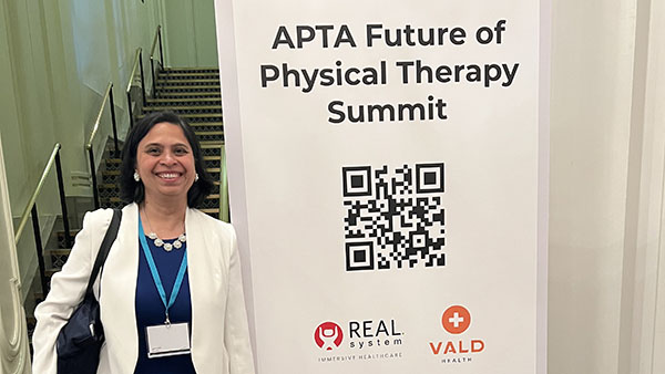 Dr. Nupur Hajela standing next to white banner that reads APTA Future of Physical Therapy Summit.