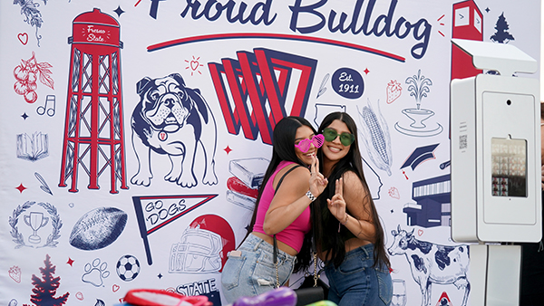 Two female students pose for a photo in front of a wall that says Proud Bulldog.
