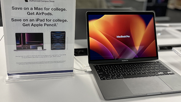 MacBook sitting on a counter next to sign that reads Save on a Mac for college. Get Airpods. Save on an iPad for college. Get Apple Pencil.