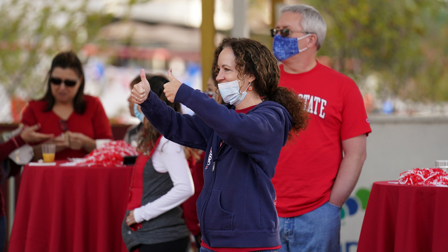Woman wearing a mask at Red Friday giving two thumbs up.