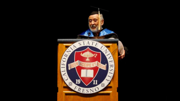 Ernesto Palomino in cap and gown standing behind a Fresno State podium.