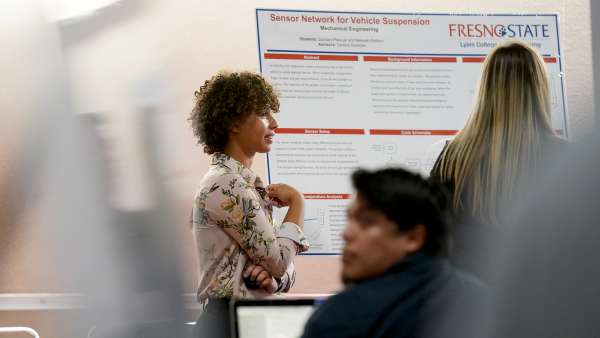 Student stands in front of research poster.