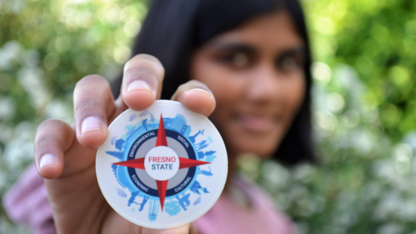 woman holds a medallion of the Fresno State sustainability logo.