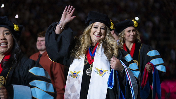 Female doctoral student smiling and waving among other students.