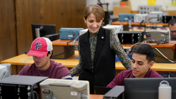 Photo of Fresno State professor standing over students at a desk.