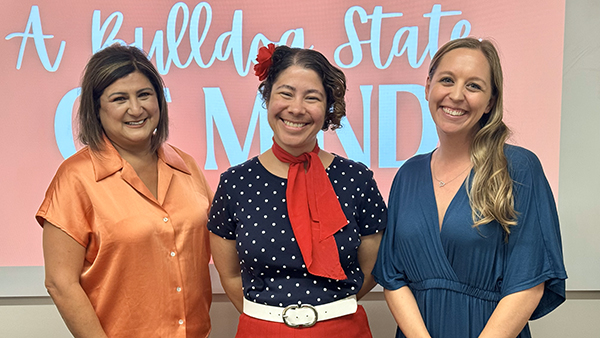 Three women standing in front of a sign that says A Bulldog state of mind