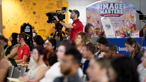 Employees listening to a lecture with vendors behind them.