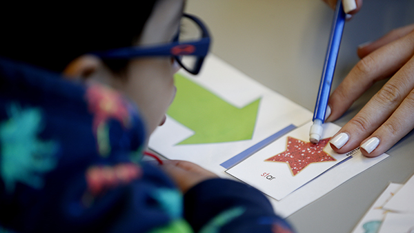 An adult uses a pencil to point to a flash card of a red star while a child looks on.