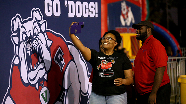 A woman taking a selfie in front of a Go 'Dogs backdrop with the four paw Bulldog.