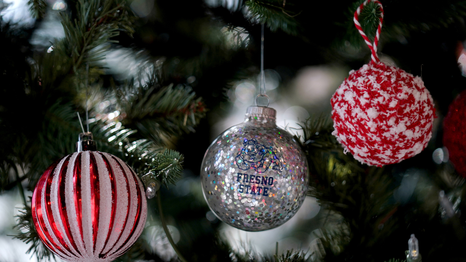 Holiday ornaments on a tree, one has the bulldog and Fresno State on it