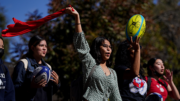 Female students at Fresno State waving a red T-shirt, holding Rugby balls.