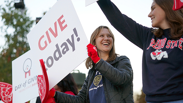 Students and staff hold "Give today!" sign and cheer for the annual Day of Giving event.