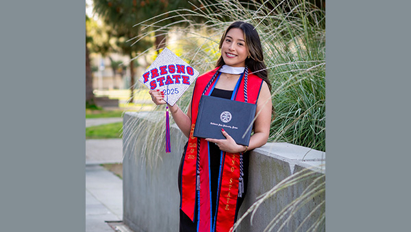 Itzel Montoya holding a degree folder and a mortar board with the words Fresno State on it.