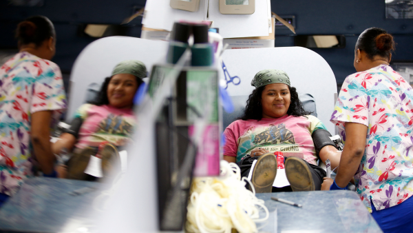 Student lays on a bed with a blood pressure cuff around her arm while a nurse looks on.