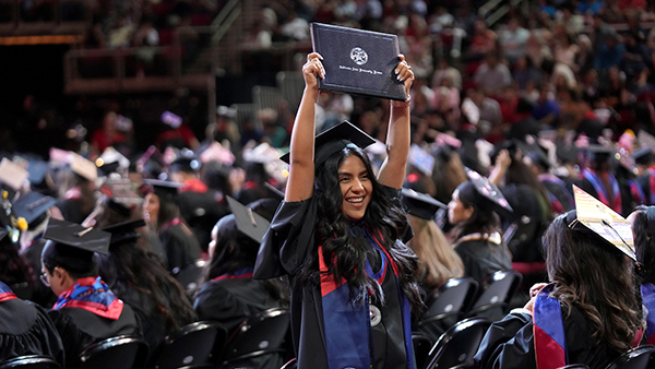 Woman smiling while holding diploma over her head at commencement.