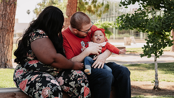 Fresno State student parents sitting on bench with their baby in the Peace Garden