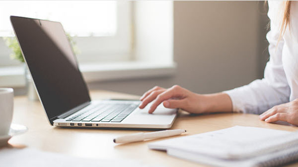Woman at desk working on laptop with pen and paper