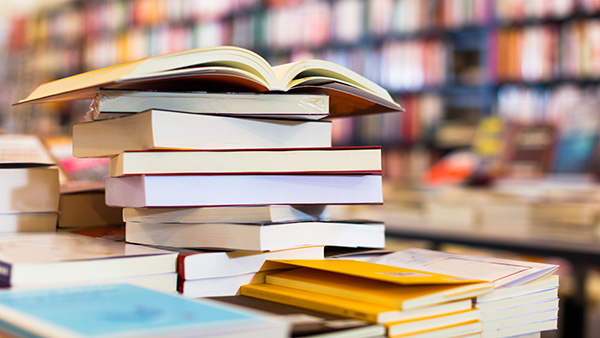 Stack of book on a table with books with shelves of books behind it.