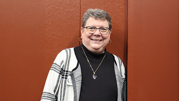 Photo of Pam Dyer in front of a brick red-colored wall.