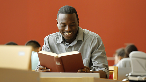 African American student reading a book in the library.