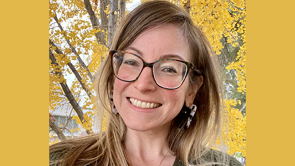 Beth Wilkinson in front a tree with yellow flowers.