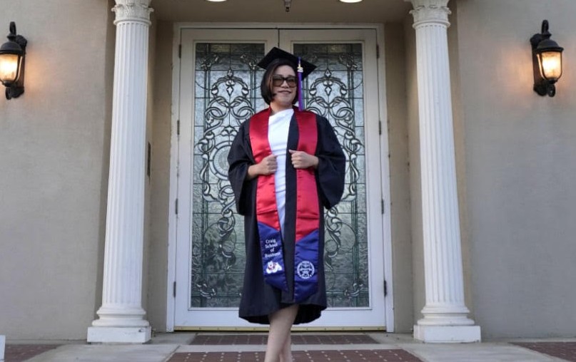 Maria Jacinto posing in graduation regalia in front of Smittcamp Alumni House