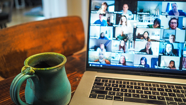 Teal coffee mug next to a laptop with a virtual meeting on the screen.