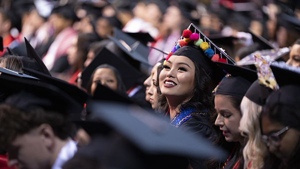 Female Hmong student in graduation robes staring off to the stands in the Save Mart center.