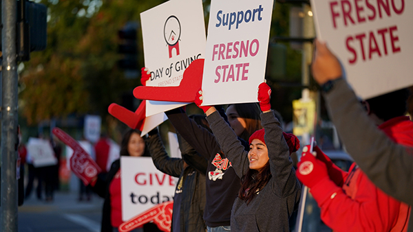 Volunteers in red gloves and beanies holding signs that say support Fresno State.