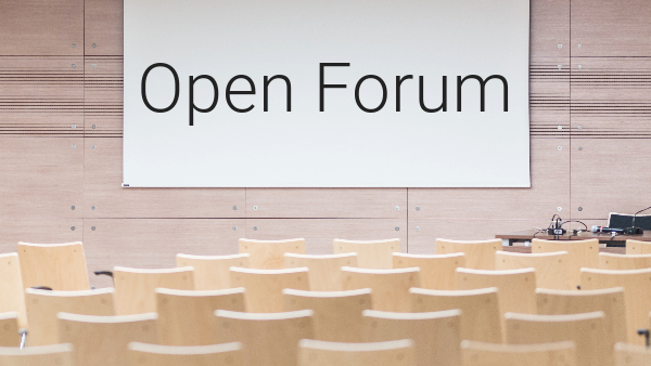 A meeting room with light wood chairs. A screen in the front of the room reads open forum.