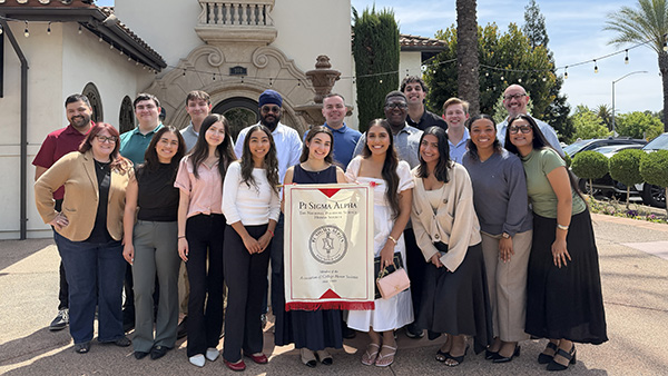 Multiple members of Pi Sigma Alpha, with a banner of their organization in front, standing in front of a building