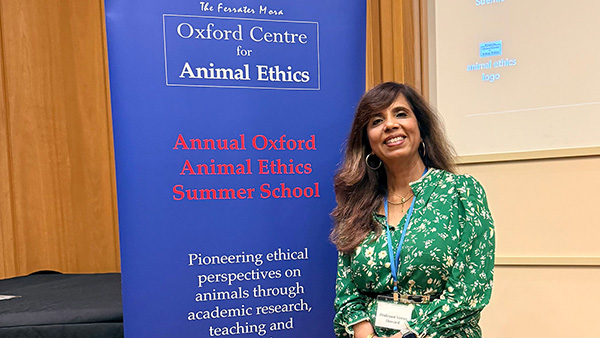 Dr. Veena Howard standing next to a banner that say "Oxford Centre for Animal Ethics".