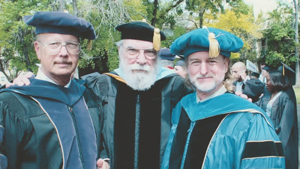 Dr. Max Futrrell (center) in commencement robes and two others standing beside him..