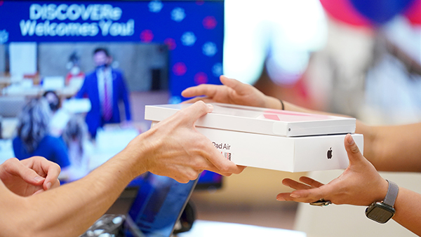 Two people grabbing an iPad box at the DISCOVERe desk.