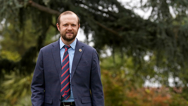 Dr. Robert Lull in a navy jacket with red and blue striped tie with trees behind him.