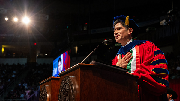President Sa&uacute;l Jim&eacute;nez-Sandoval stands at a podium with commencement robes on.