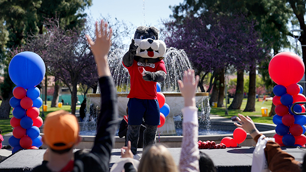 TimeOut in front of the fountain with balloons on either end. People hold their hands up.