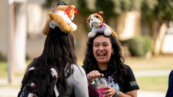 Students speaking to each other with stuffed Bulldogs on their heads.