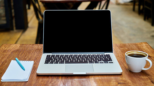 Laptop with a pen and paper on the left and a cup of coffee on the right